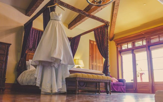 Wedding dress hanging on the corner of a four-poster bed with French doors to the outside