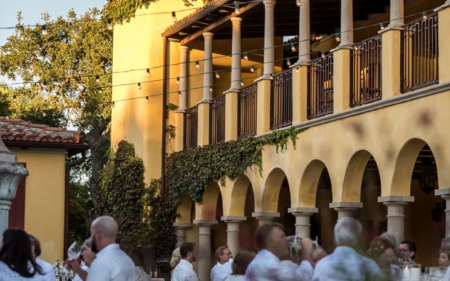 Italian villa style building with tower and diners seated at tables on the patio all dressed in white